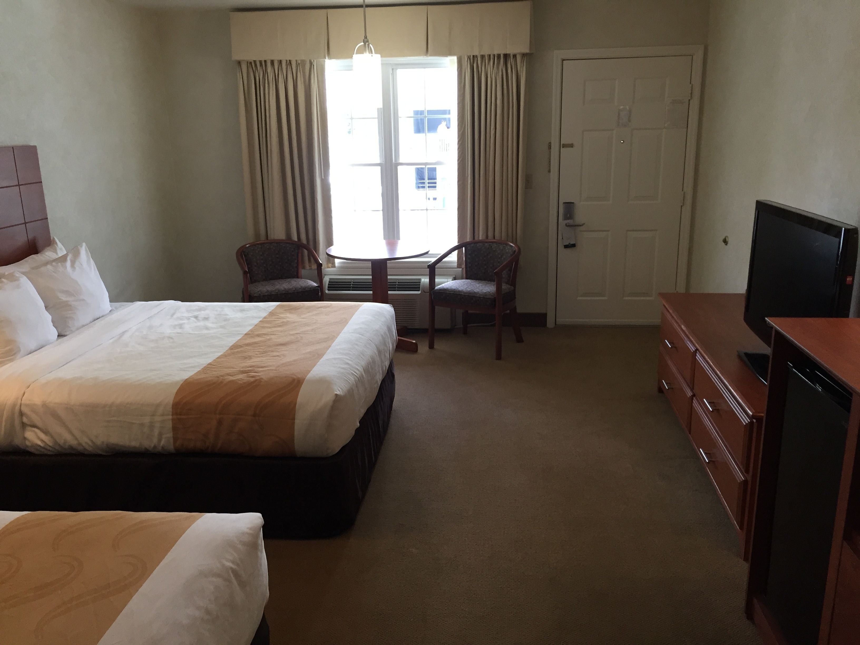 A hotel room with a large bed, two chairs, a small table, a TV, and a wardrobe.