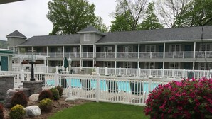 A two-story building with a pool, white railings, and a garden with rocks and flowers. - Quality Inn Lake George (Lake George)
