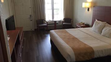 Habitación de hotel con una cama grande, dos sillones, un escritorio, un televisor y una ventana con cortinas.