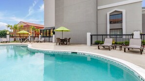 A swimming pool with lounge chairs and umbrellas, surrounded by a building with a modern design. - Sleep Inn Orangeburg (Orangeburg)