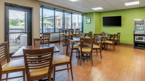 A dining area with wooden tables and chairs, a large window with a view, a flat-screen TV, and a vending machine. - Sleep Inn Orangeburg (Orangeburg)