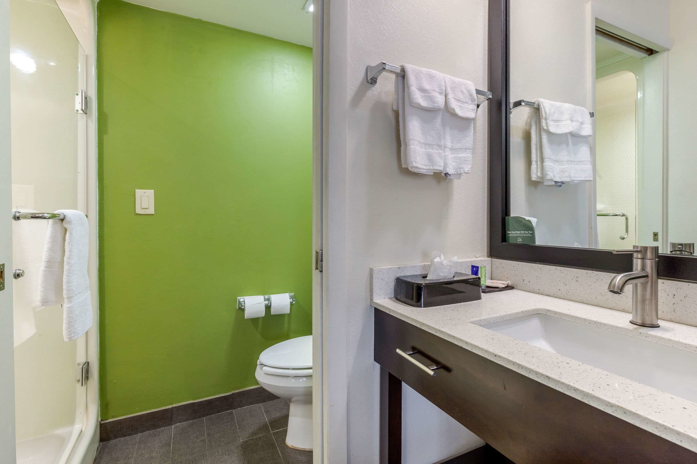 A bathroom with a green wall, white toilet, and a sink with a mirror.