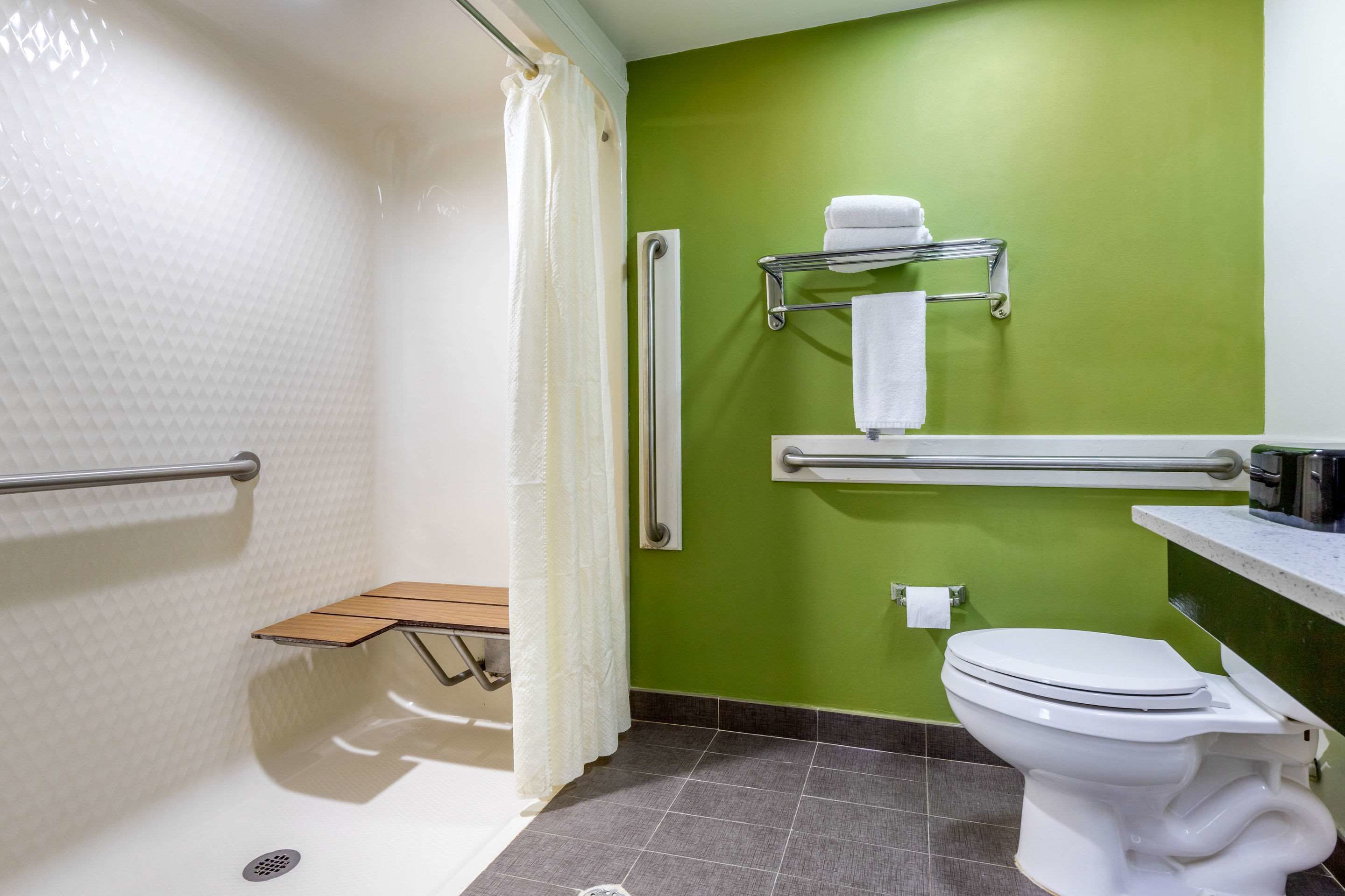 A bathroom with a shower, grab bars, a toilet, and a towel rack.