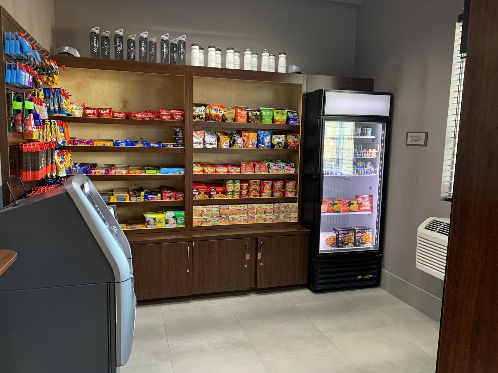 A small convenience store with shelves stocked with snacks, beverages, and a refrigerated display case.