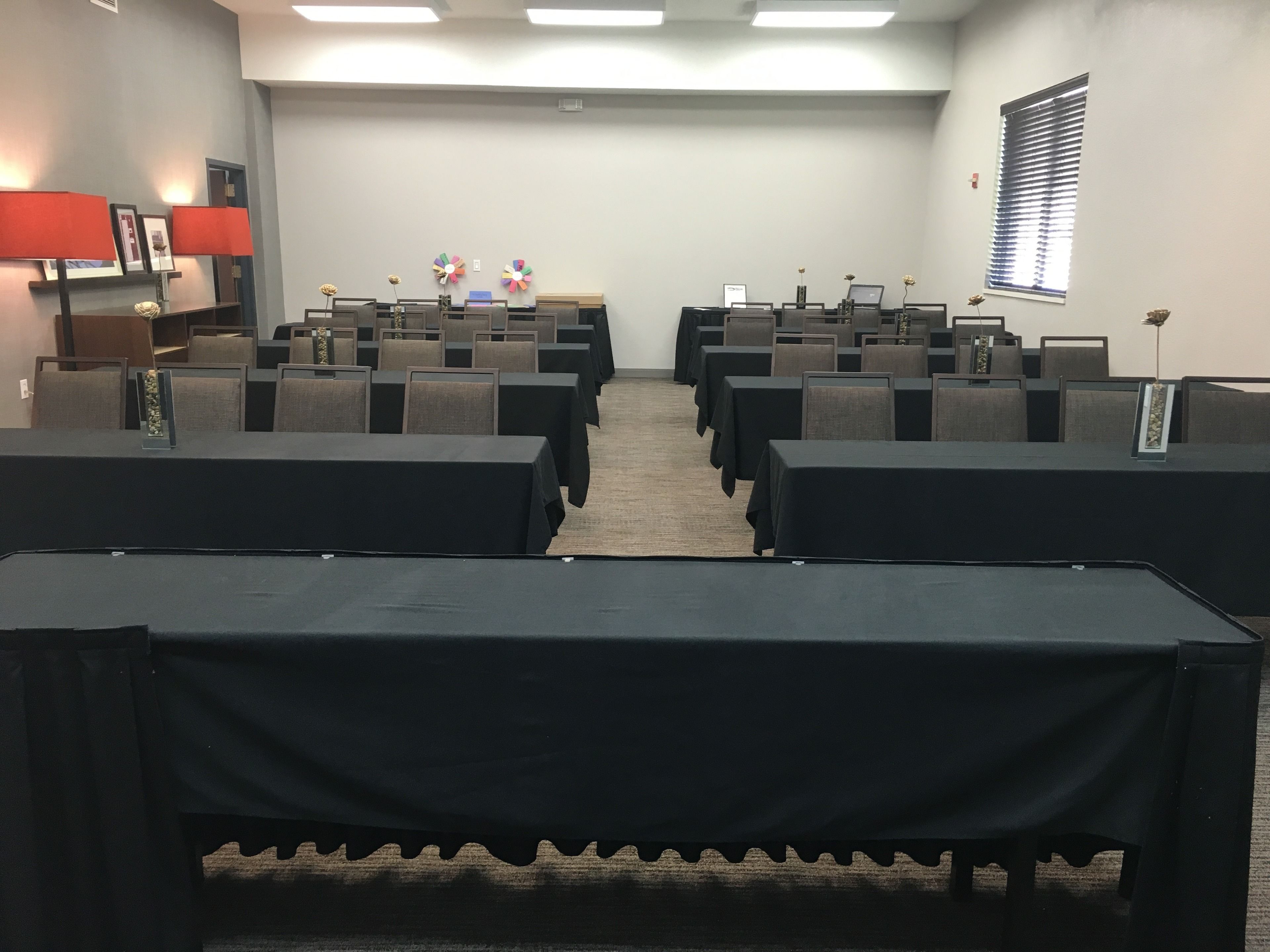 Une salle de conférence avec des rangées de tables et de chaises, un écran de projection et une fenêtre équipée de stores.