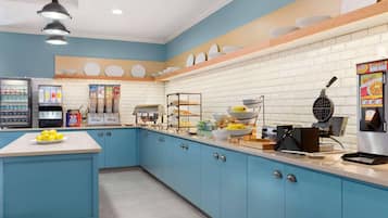 A kitchen with blue cabinets, a white countertop, a waffle maker, and a beverage dispenser.