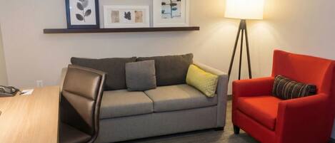 A room with a grey sofa, a red armchair, a desk with a phone, and a floor lamp.