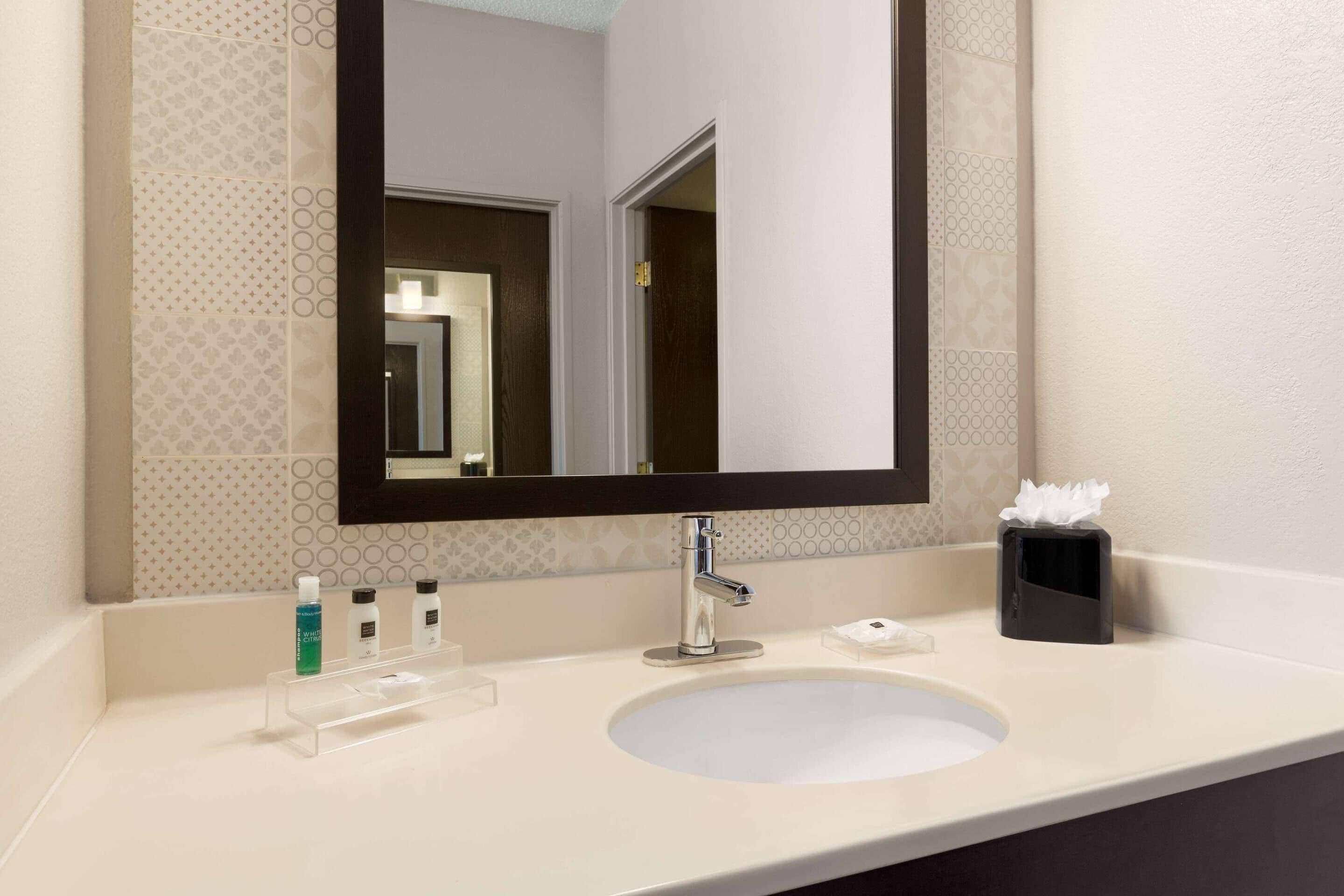 A bathroom with a white sink, a mirror, and toiletries on the counter.