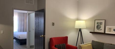 A hotel room with a bed, a red armchair, a floor lamp, a sofa, and a ceiling fan.