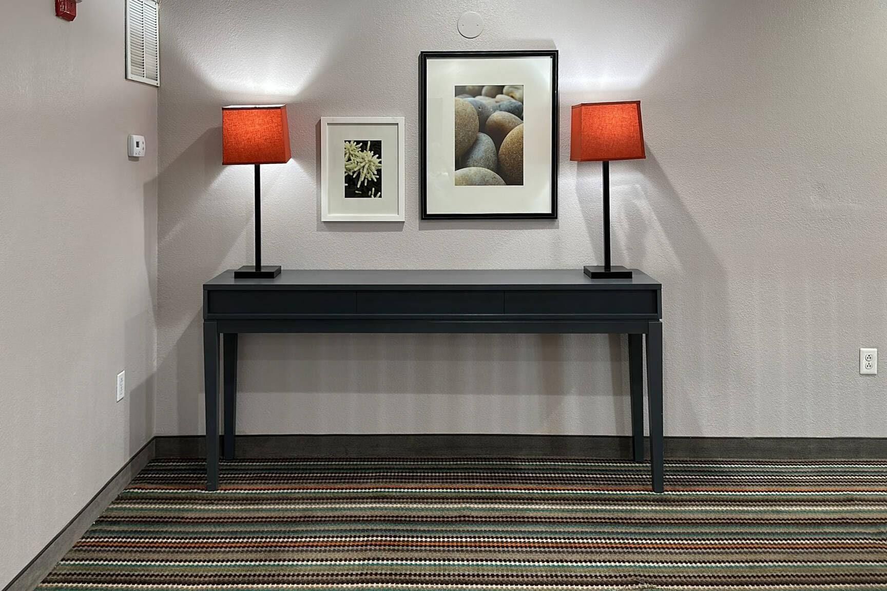 A hallway with a black console table, two red lamps, and two framed pictures on the wall.