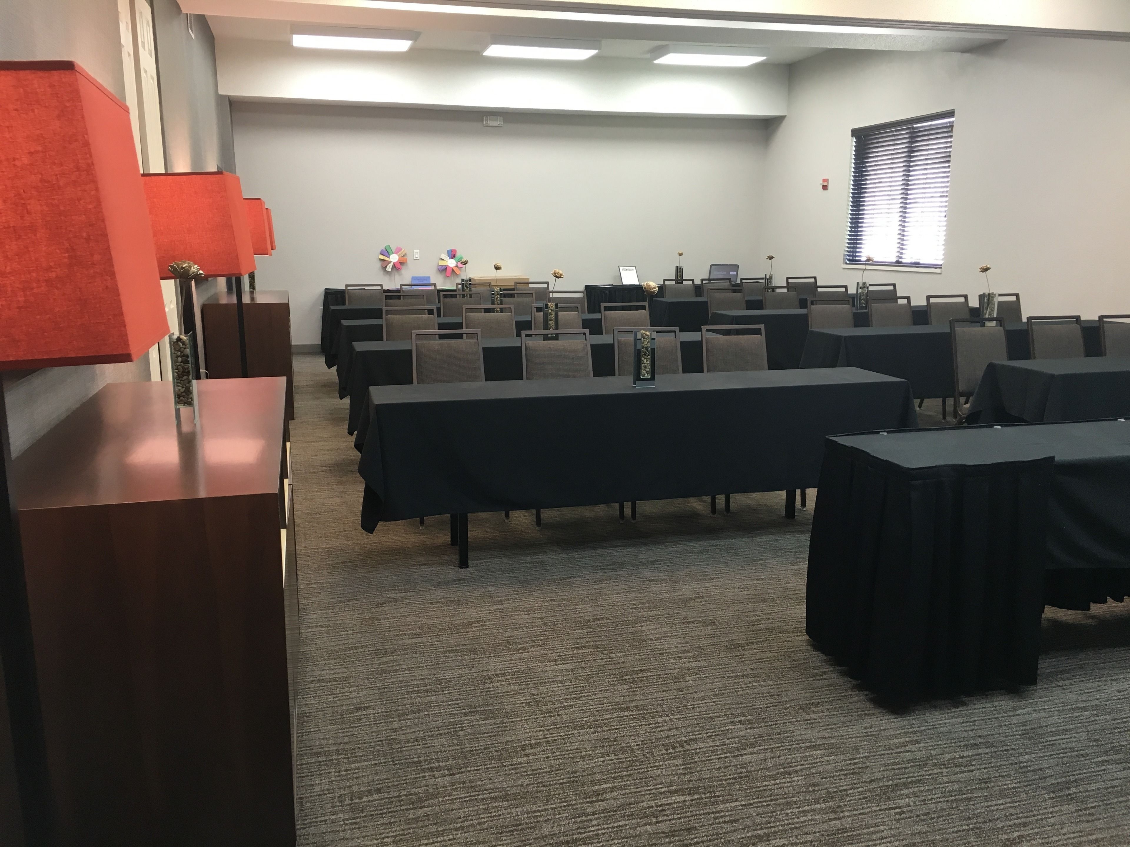 A conference room with multiple tables and chairs, a podium, and a window with blinds.