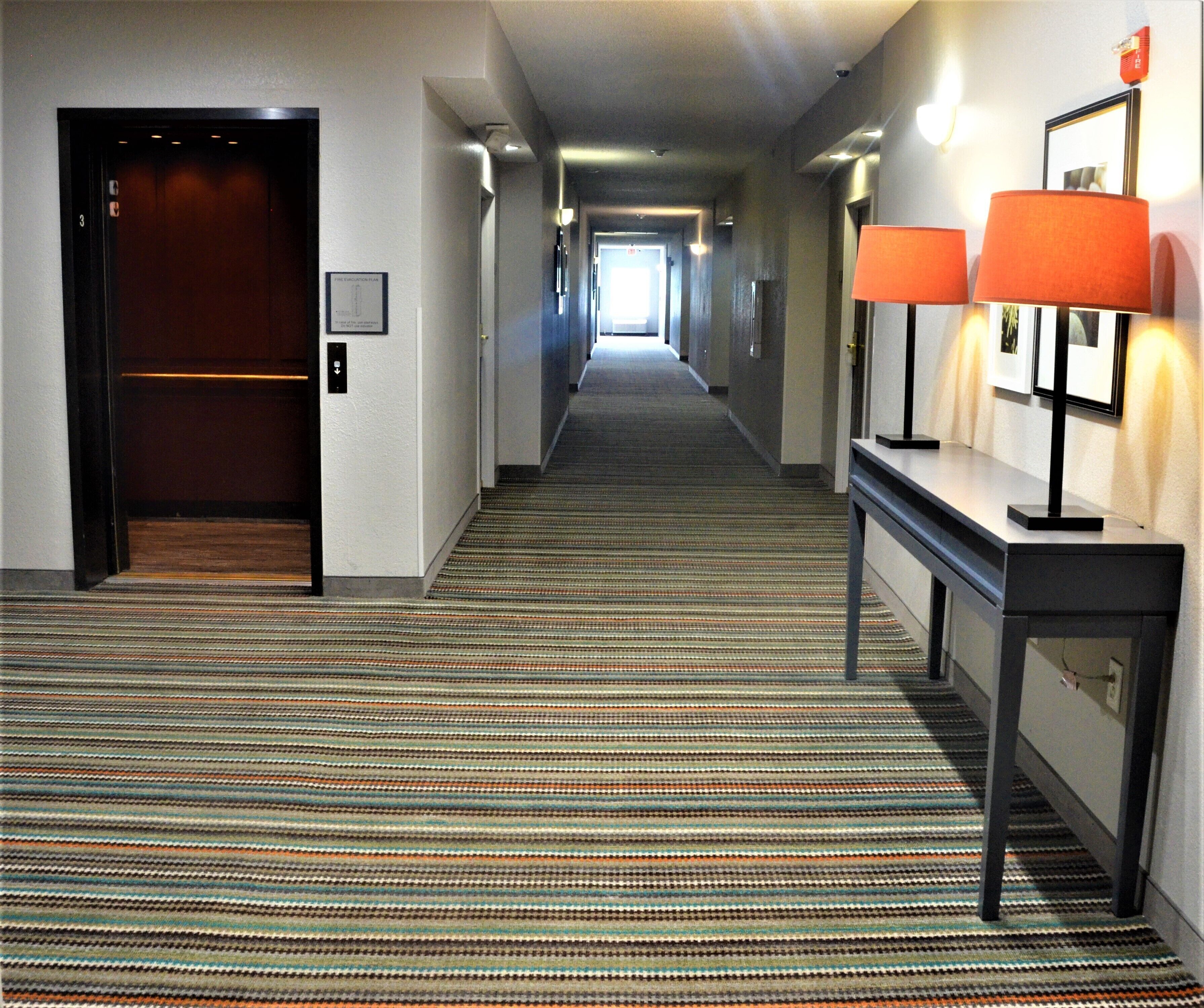 A hotel hallway with a striped carpet, a reception desk with two lamps, and an elevator on the left.