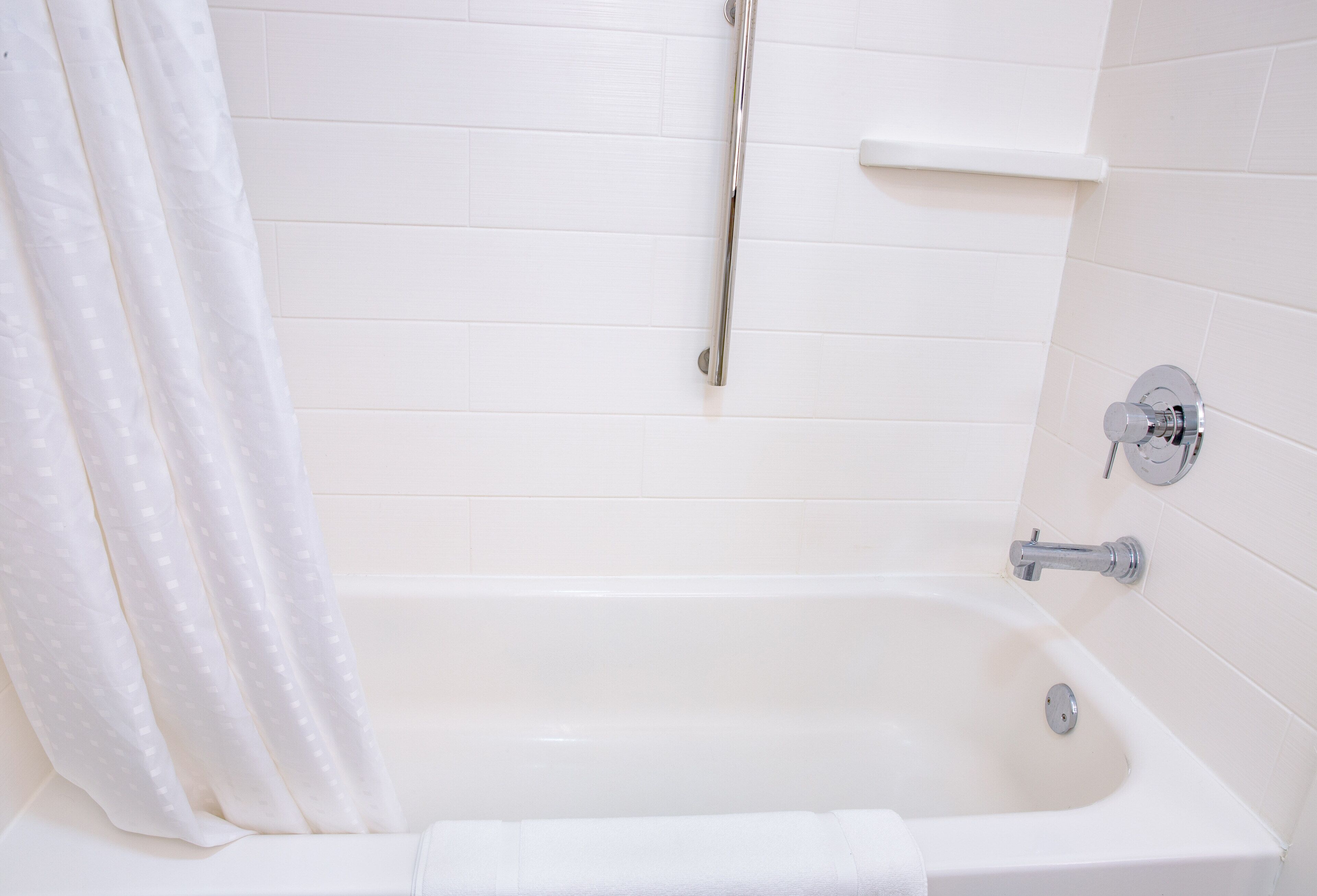Una vasca da bagno bianca con tenda da doccia, soffione manuale e rubinetto a parete.