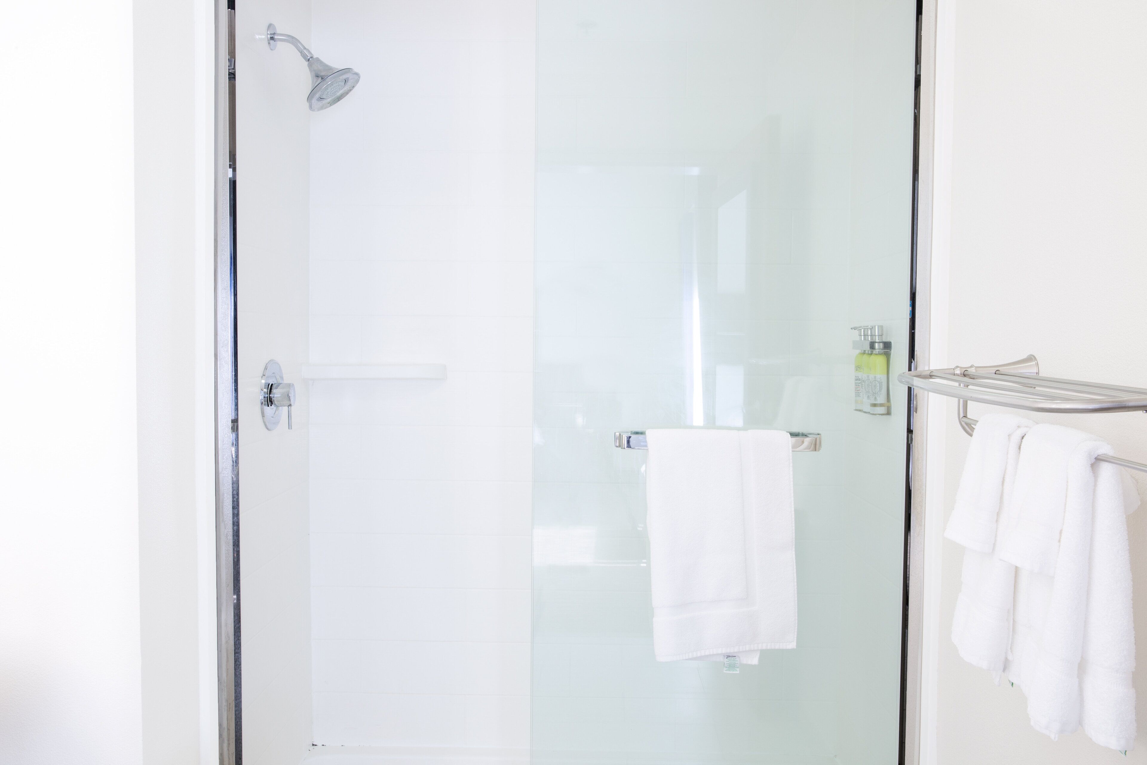 A glass-enclosed shower with a handheld showerhead, a glass door, and a towel rack with multiple white towels.