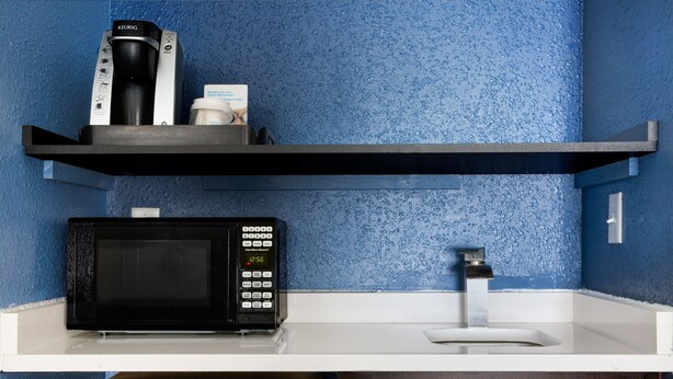 Una kitchenette equipada con microondas, cafetera y un lavamanos pequeño.