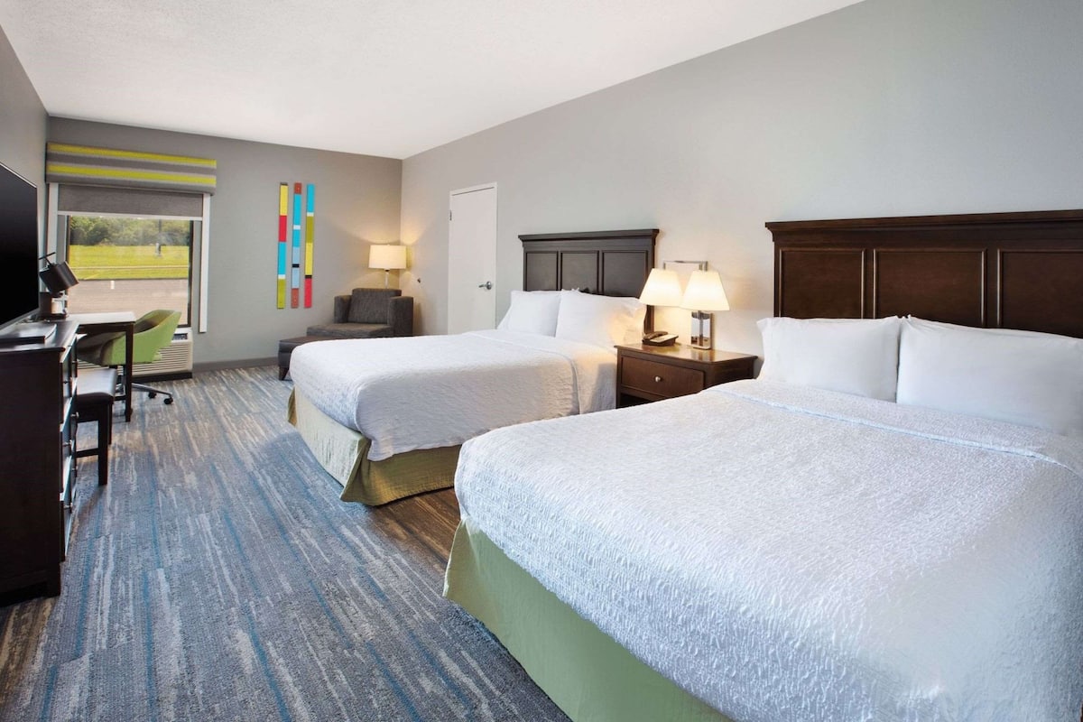 A hotel room with two beds, a desk, a chair, and a TV.