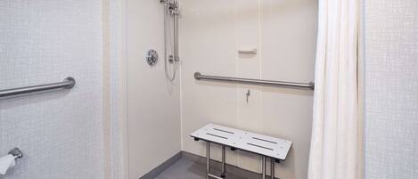 A small, enclosed shower area with a grab bar, a bench, and a towel dispenser.
