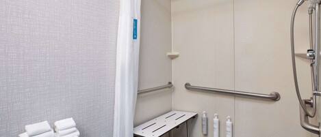 A shower area with a grab bar, a towel rack, and a shelf with toiletries.