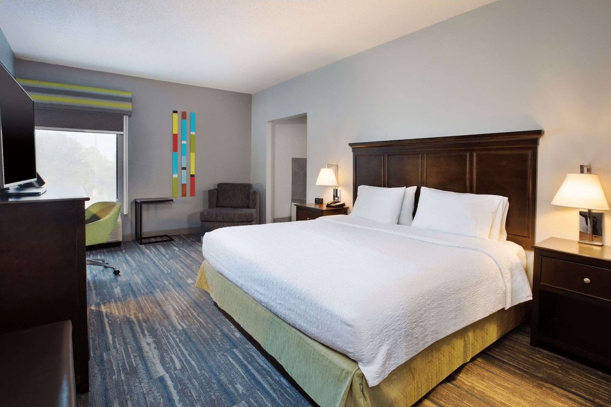 A hotel room with a large bed, a desk, a chair, and a TV.