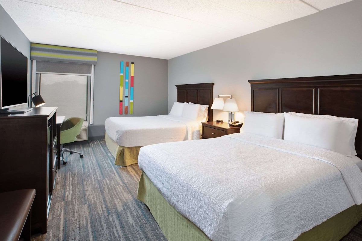 A hotel room with two beds, a desk, a chair, and a TV.