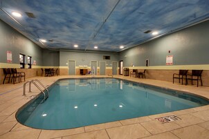 Piscina interior com água cristalina, rodeada por pavimento e paredes revestidas de azulejos bege.