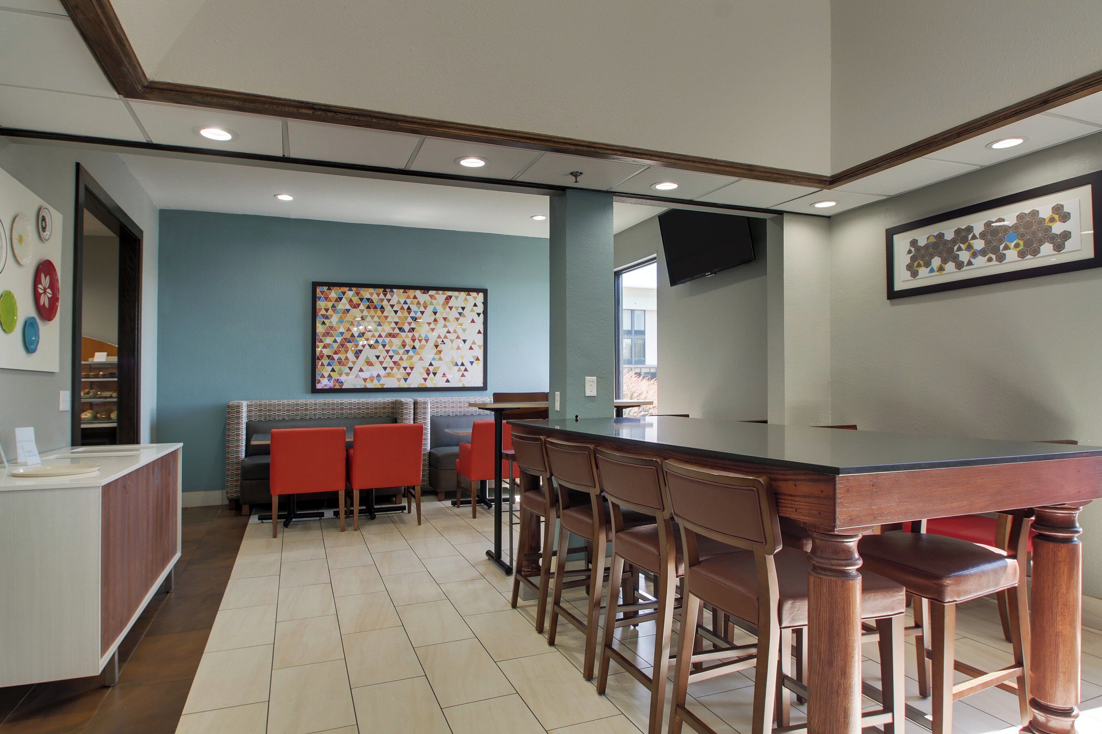 A restaurant with a long counter, multiple chairs, and a wall with a colorful geometric pattern.