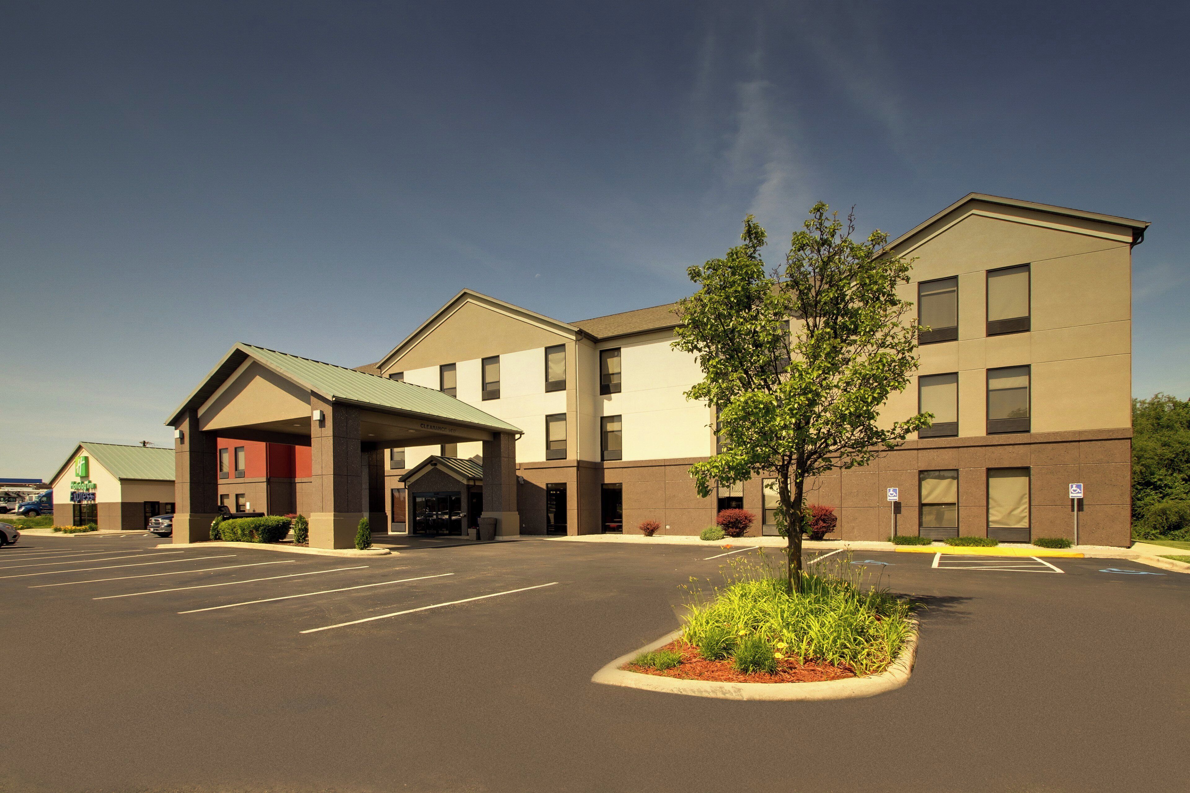 A hotel with a parking lot, a covered entrance, and a landscaped area with a tree.