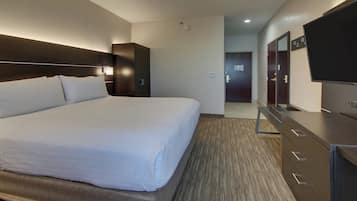 A hotel room with a large bed, a dresser, a flat-screen TV, and a door leading to a hallway.
