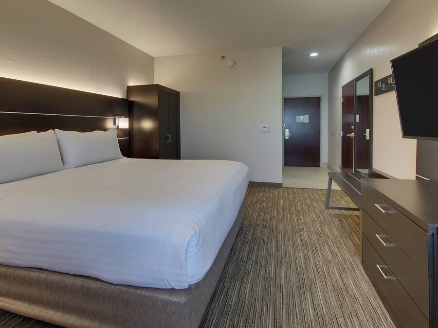 A hotel room with a large bed, a dresser, a flat-screen TV, and a door leading to a hallway.