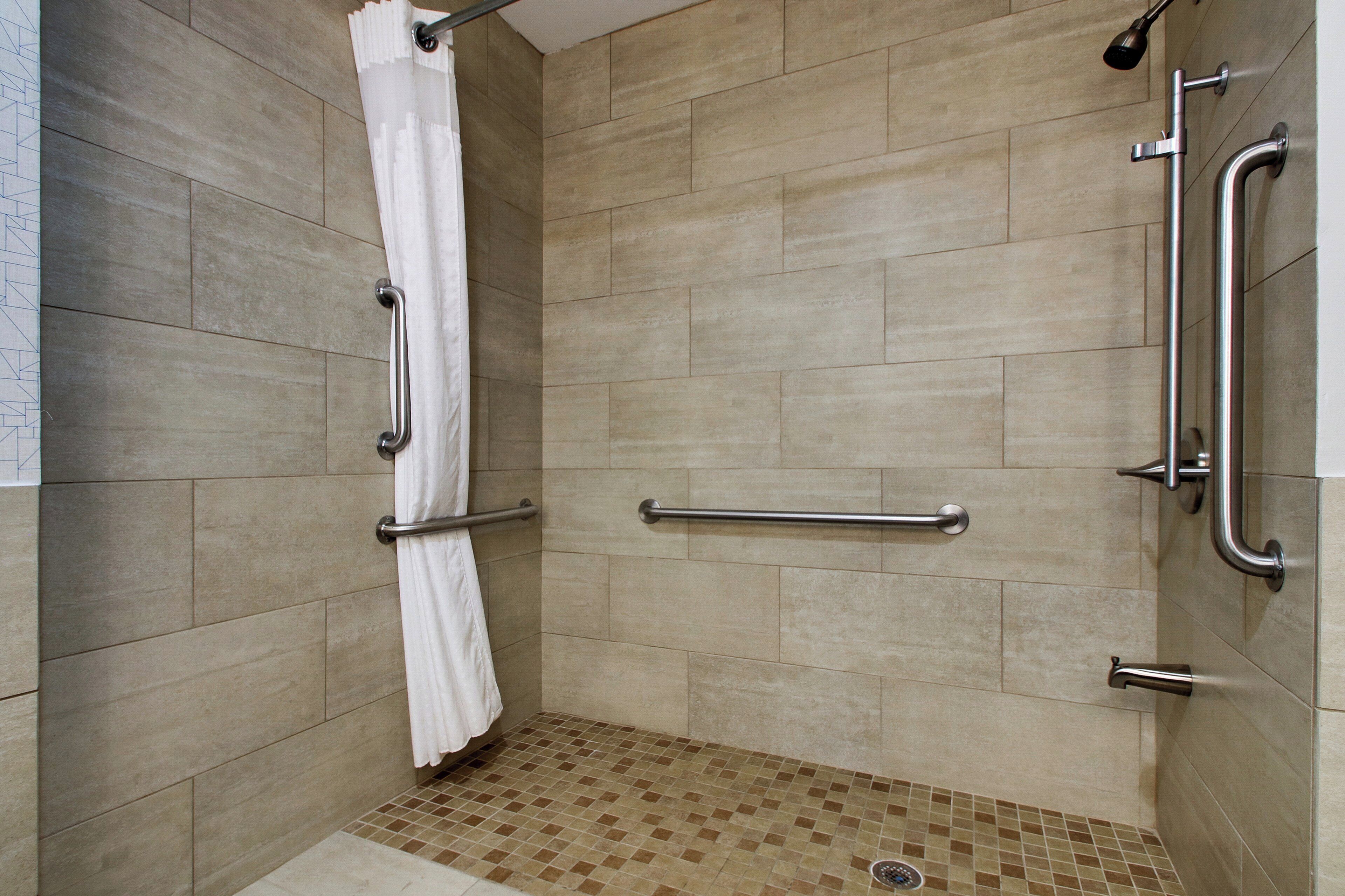 A shower with grab bars and a tiled floor.