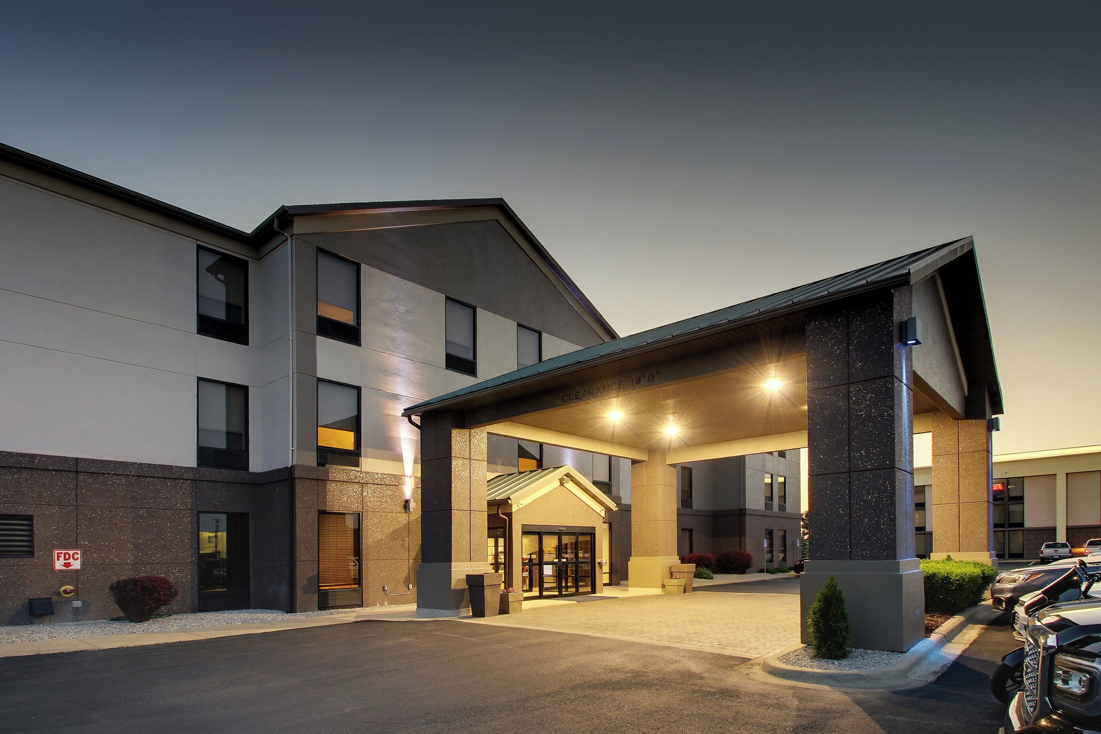 A modern hotel entrance with a covered driveway and a parking area.