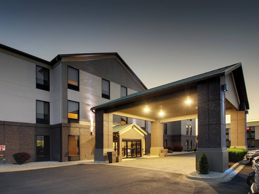 A modern hotel entrance with a covered driveway and a parking area.