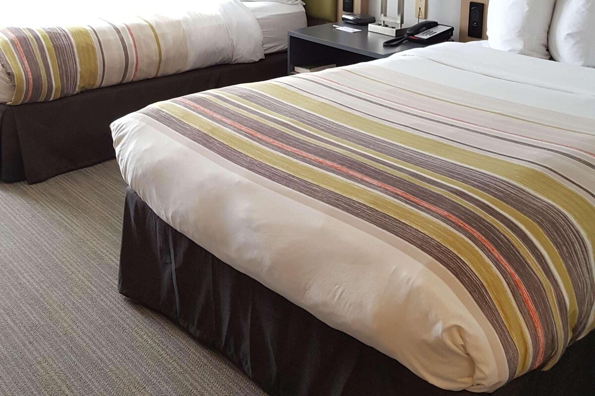 A hotel room with two beds, each with a striped bedspread, a nightstand with a lamp, and a window with curtains.