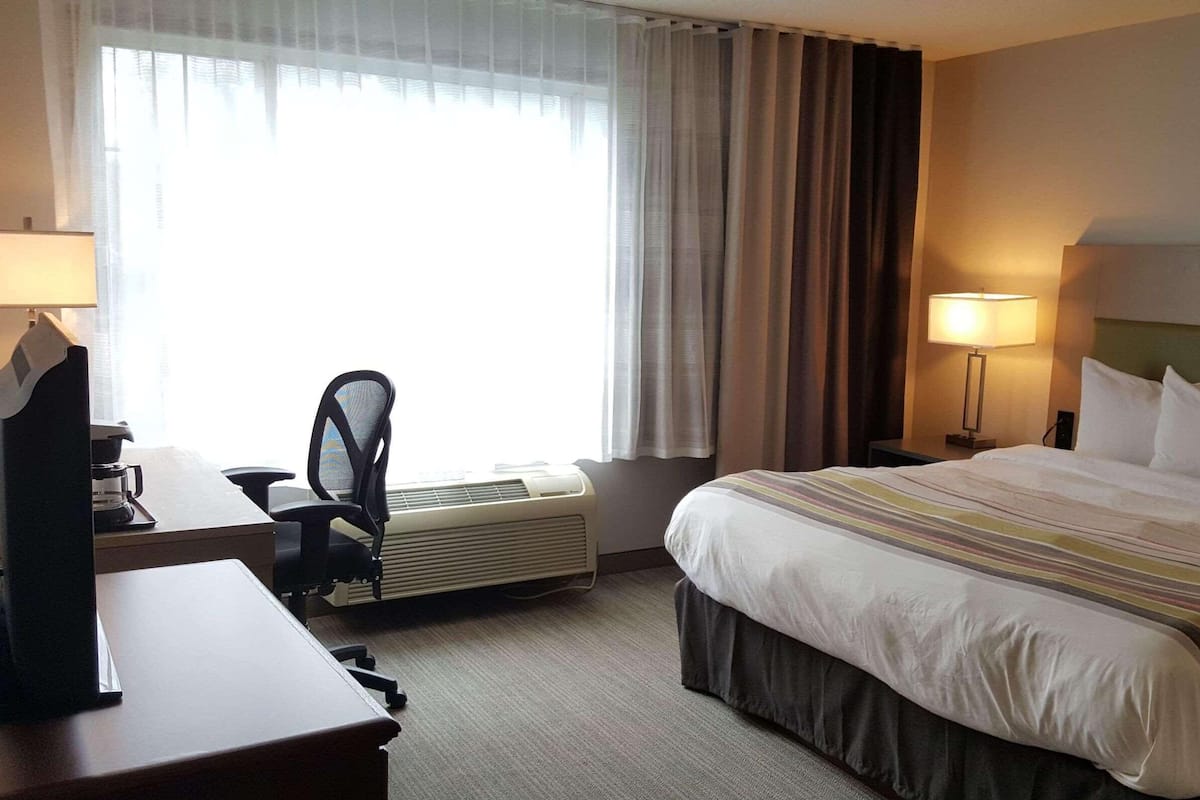 A hotel room with a bed, desk, chair, and a window with curtains.