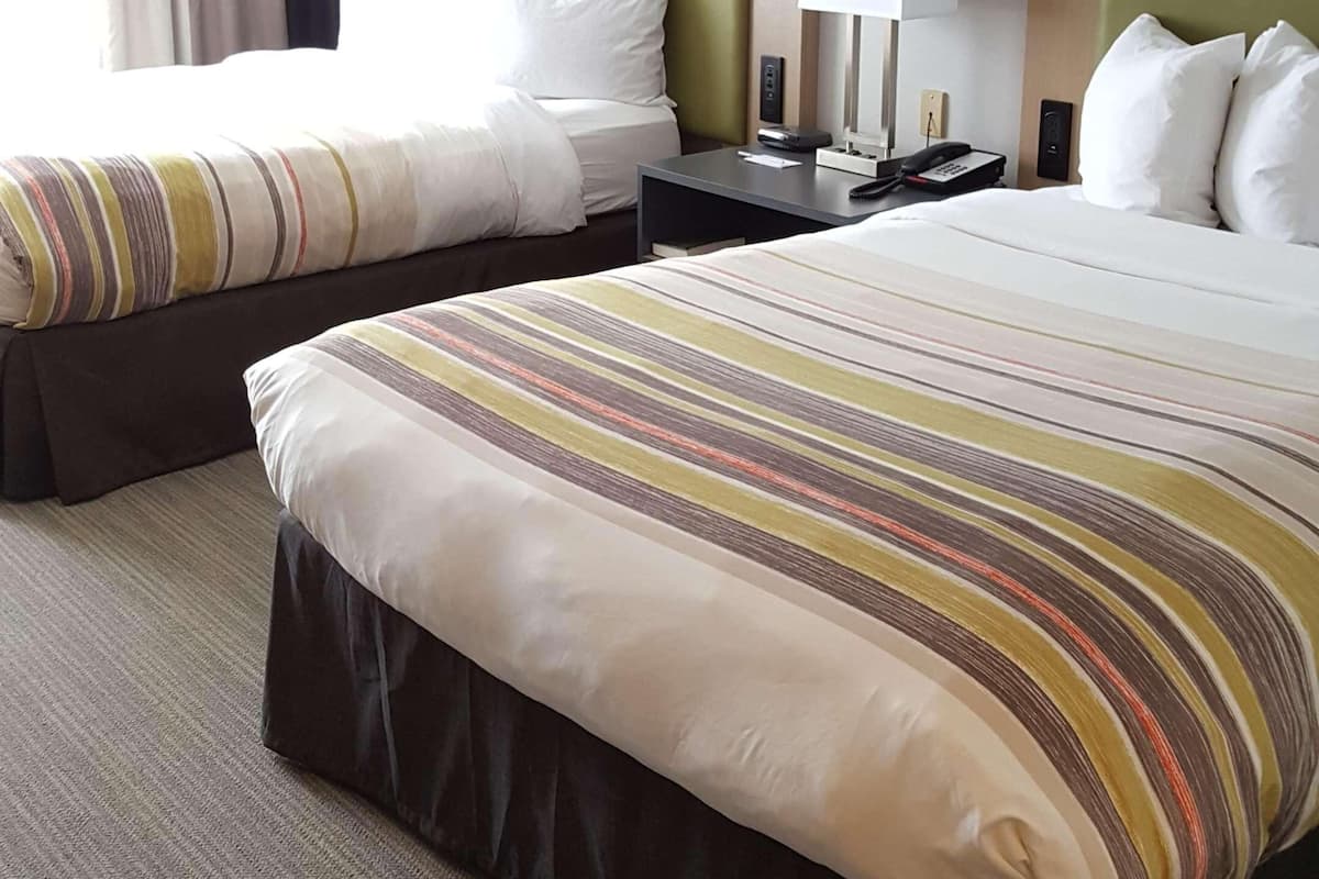 A hotel room with two beds, each with a striped bedspread, a nightstand with a lamp, and a wall-mounted phone.