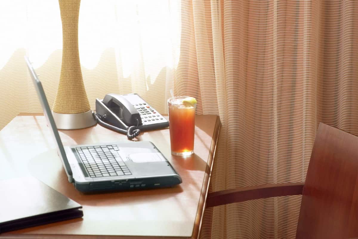 A hotel room with a wooden desk, a laptop, a telephone, and a glass of orange juice.