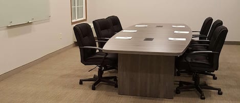A conference room with a large table, black chairs, a whiteboard, and a flat-screen TV on the wall.