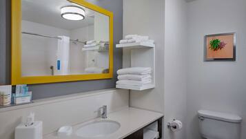 Un baño con un espejo grande, un lavabo, un inodoro y repisas con toallas dobladas.