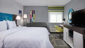 Une chambre d’hôtel avec un grand lit, un bureau doté d’un téléviseur à écran plat, une chaise, une lampe de bureau et une fenêtre donnant sur la ville.
