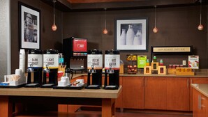 Un comptoir pour le petit-déjeuner avec des distributeurs de café et de jus, une pancarte indiquant « ICI, VOTRE PETIT-DÉJEUNER COMMENCE », et une variété d’aliments pour le petit-déjeuner.