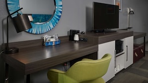 Une chambre d’hôtel équipée d’un bureau en bois, d’un grand miroir, d’un téléviseur à écran plat, d’une chaise verte, d’un four à micro-ondes et d’une machine à café.