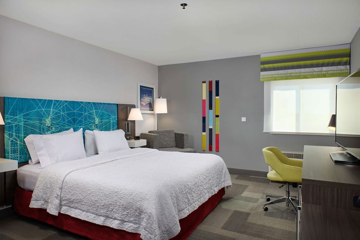 A hotel room with a large bed, a desk, a chair, a TV, and a window.