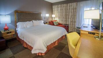 Ein Hotelzimmer mit einem großen Bett, einem Schreibtisch mit Stuhl, einem Fernseher und einer Lampe.
