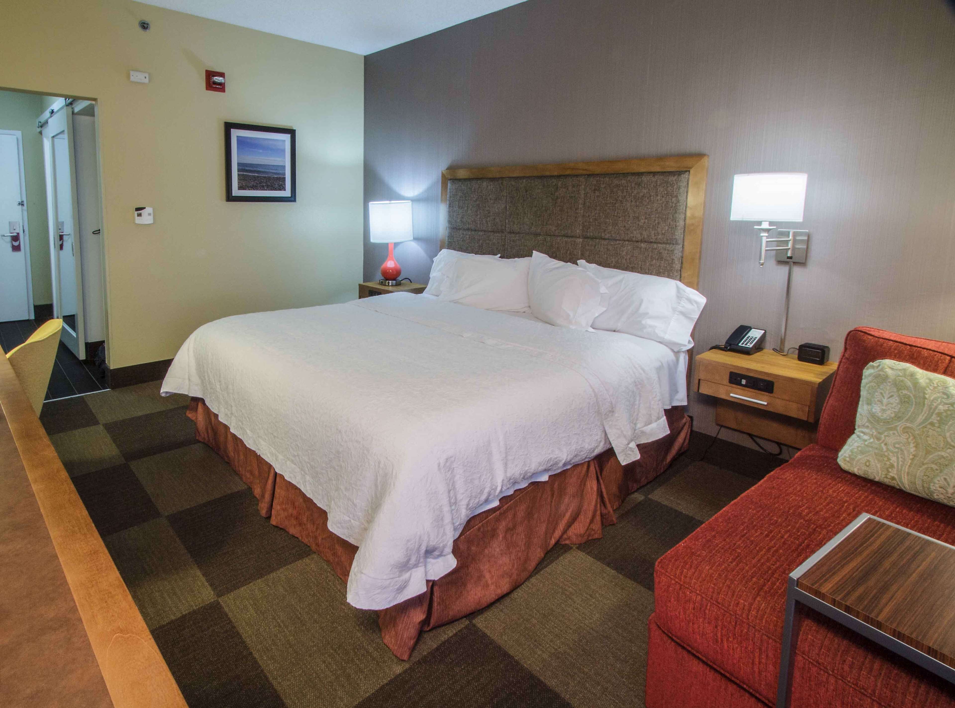 A hotel room with a large bed, a desk with a telephone, a chair, and a small table.