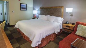 A hotel room with a large bed, a desk with a telephone, a chair, and a small table.