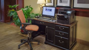 A hotel office with a desk, computer, printer, and a chair.