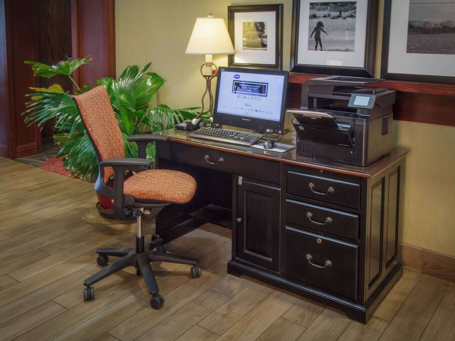 A hotel office with a desk, computer, printer, and a chair.