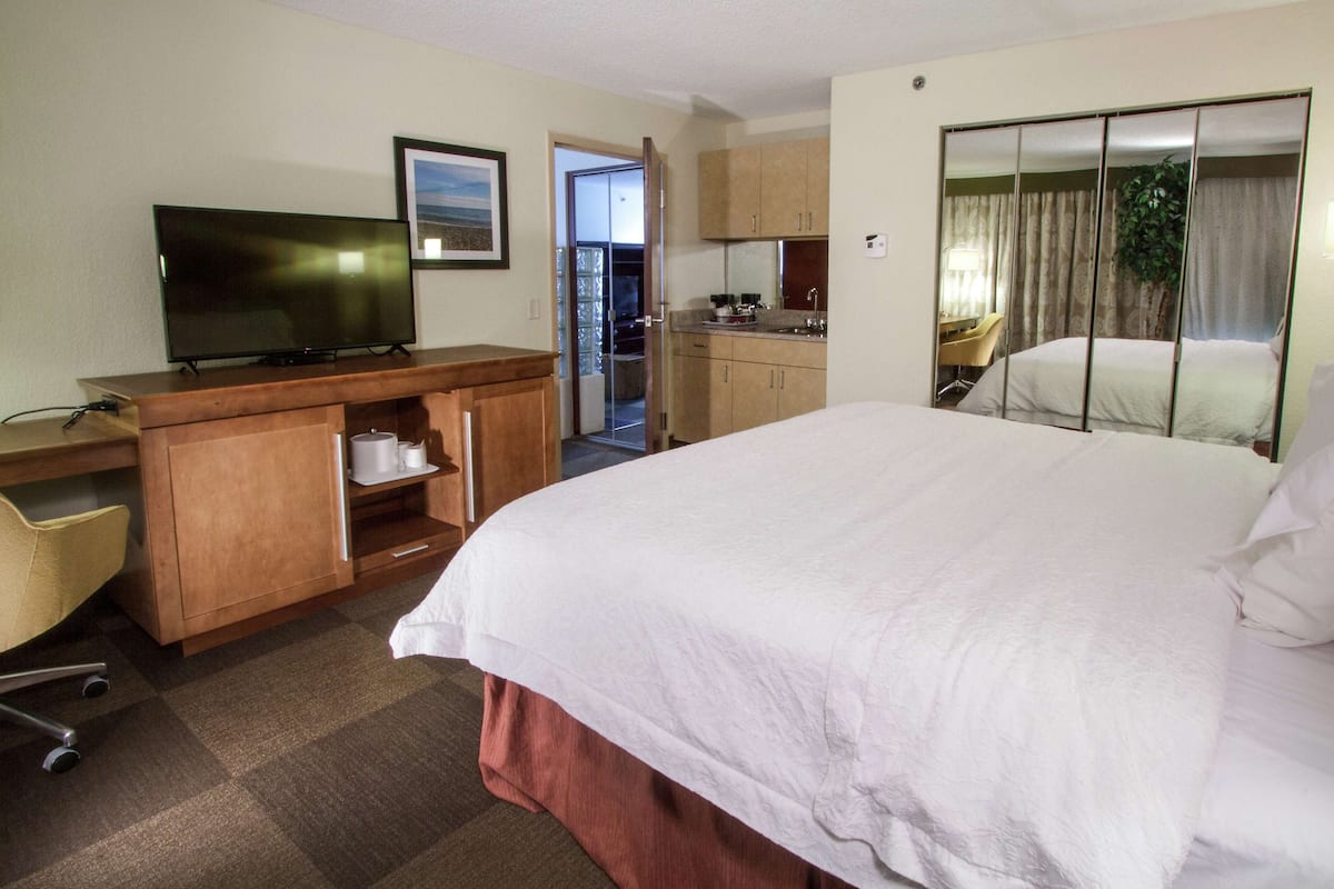 A hotel room with a bed, a desk with a television, a chair, and a bathroom visible through an open door.