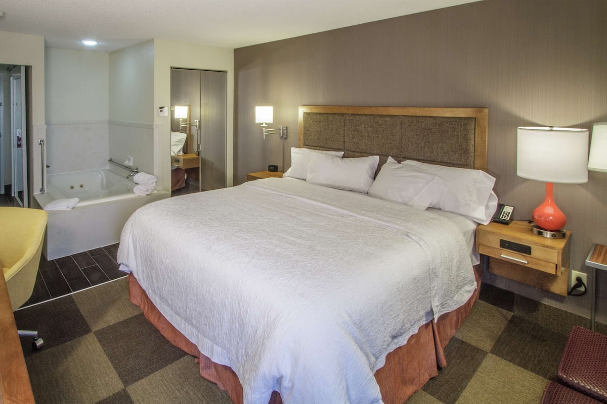 A hotel room with a large bed, a separate bathroom with a bathtub, a desk, and a chair.