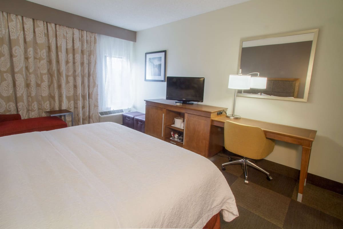 A hotel room with a large bed, a desk with a chair, a television, and a window with curtains.